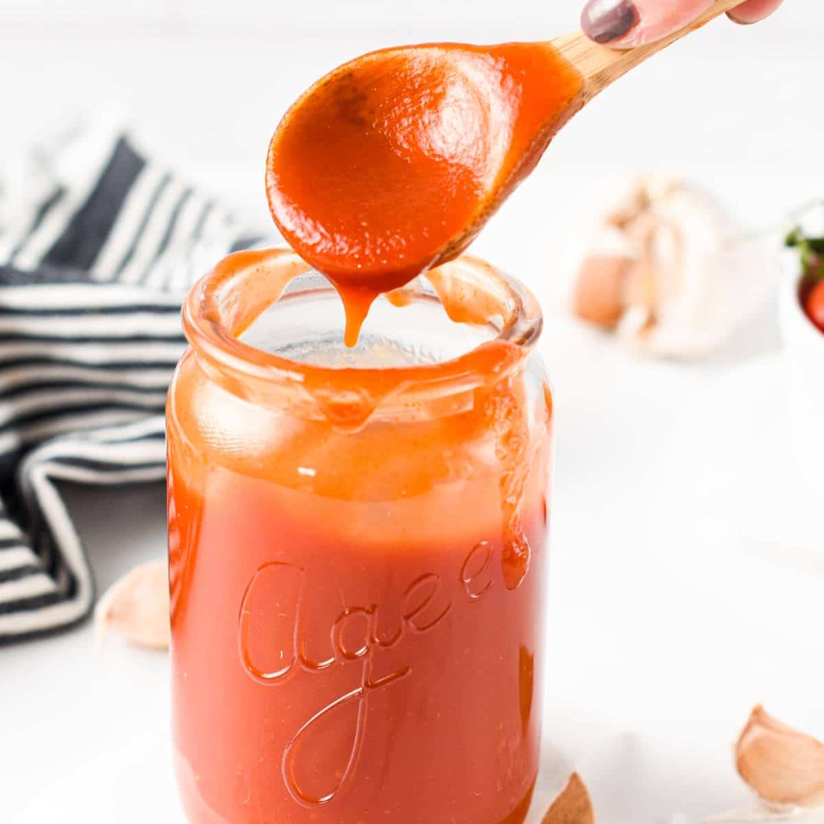 Glass jar with Homemade BBQ Sauce with 3 ingredients and a wooden spoon dripping sauce above it.