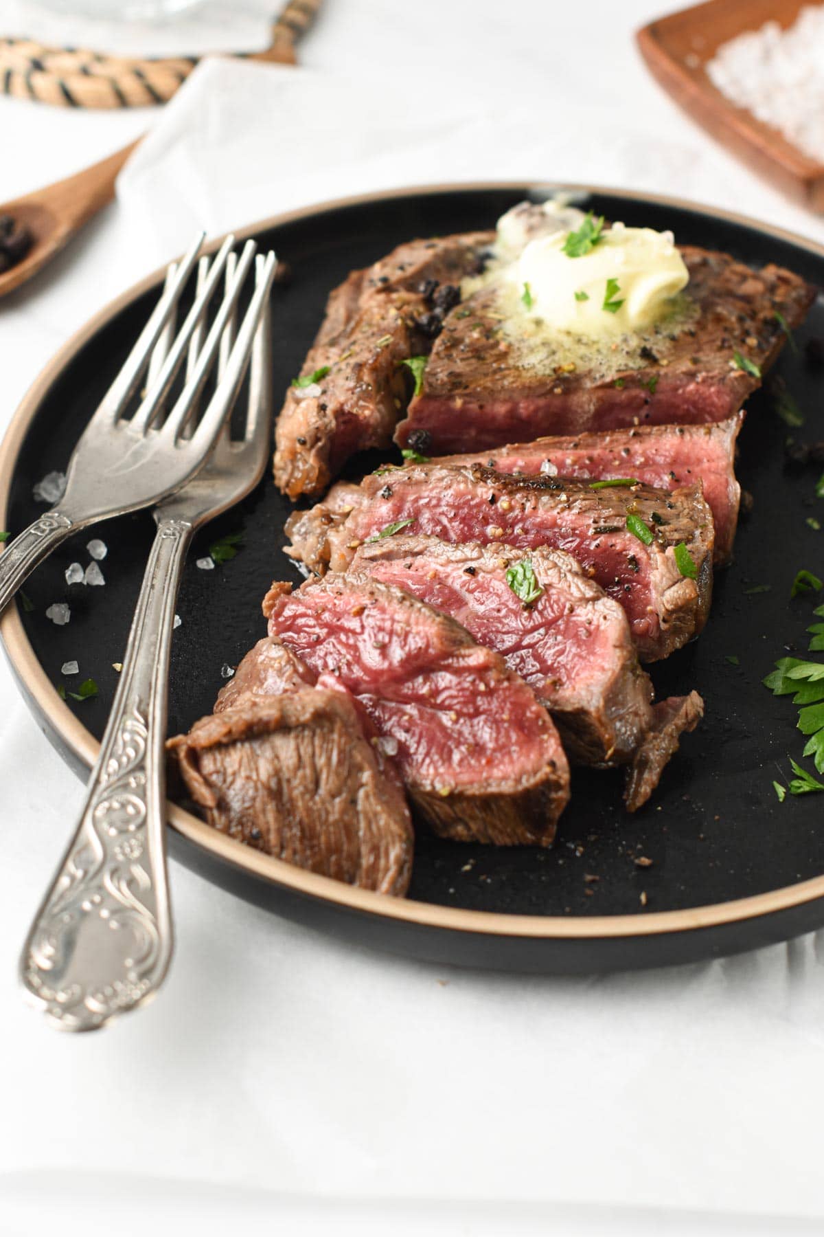 3 ingredient Steak Marinade on a cooked steak on a dark plate with silver forks.