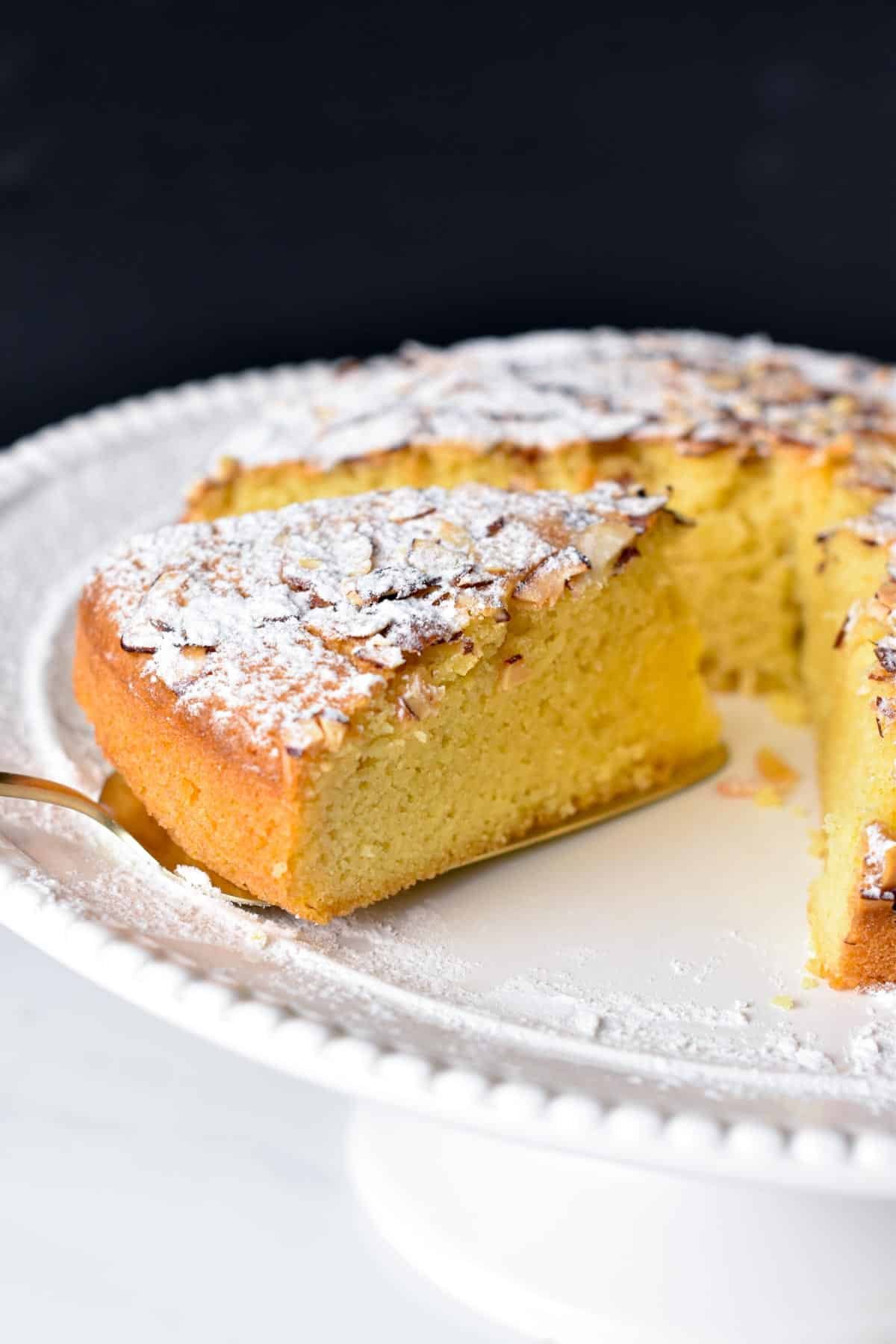 Flourless Almond Cake on a cake stand with one slice on a cake spatula.