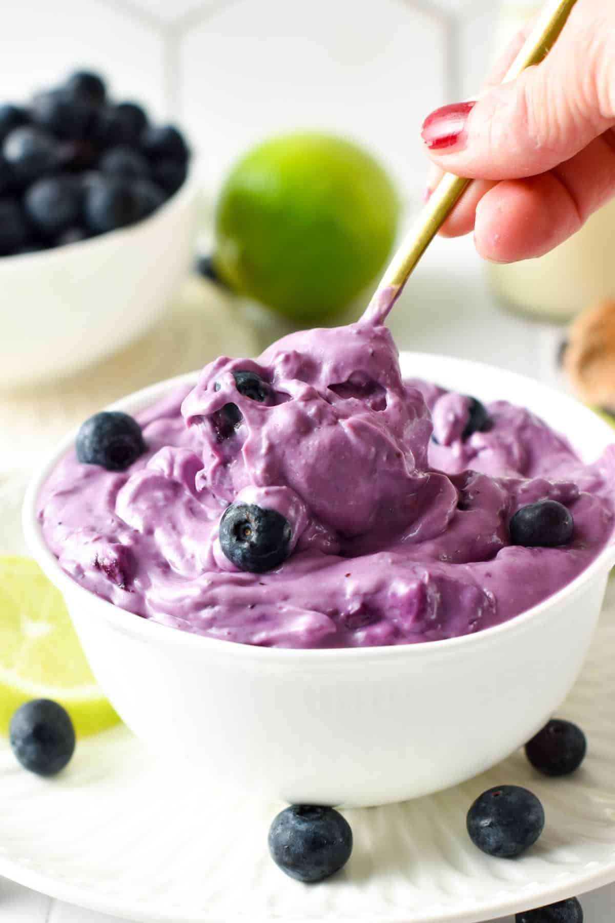 Blueberry Cream Cheese dessert in a small white bowl with a golden spoon.