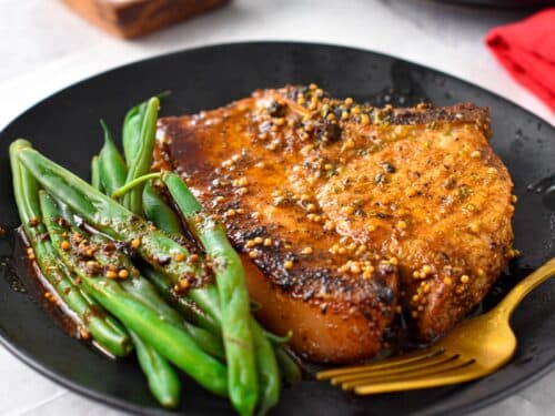 a plate with a broiled pork chop and green beans on the side