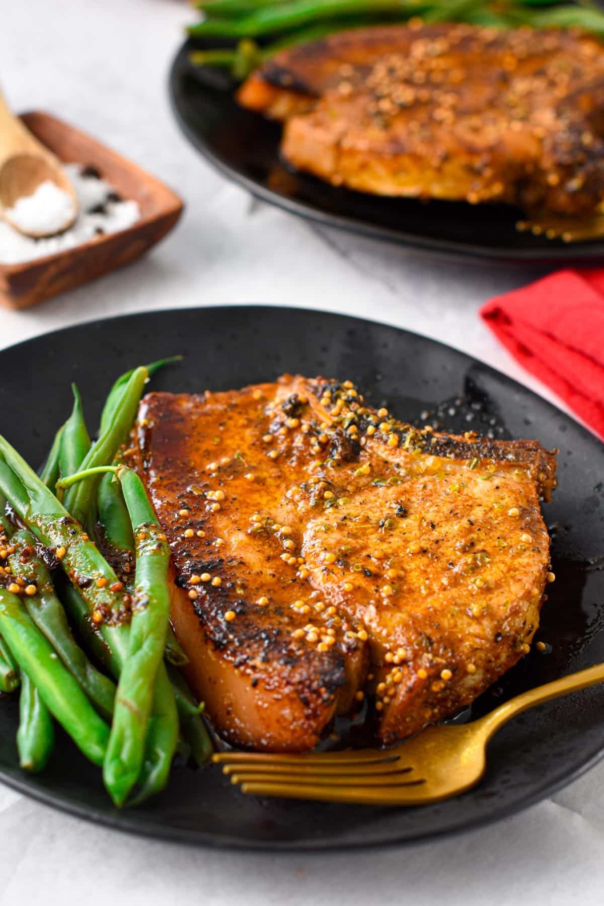A plate with a broiled pork chop and green beans on the side.