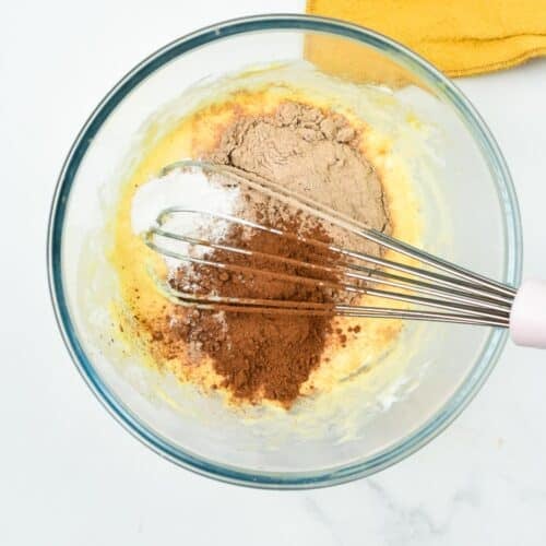a whisk whisking cocoa powder, protein powder, baking powder in a egg mixture in a mixing bowl