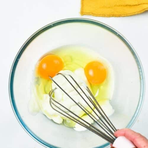 a whisk whisking eggs and yogurt in a mixing bowl