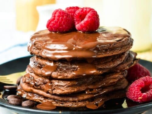 a stack of Chocolate Protein Pancakes with chocolate sauce on top and fresh raspberries
