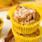 a stack of two coconut flour banana muffins with yellow muffin paper and shredded coconut on top