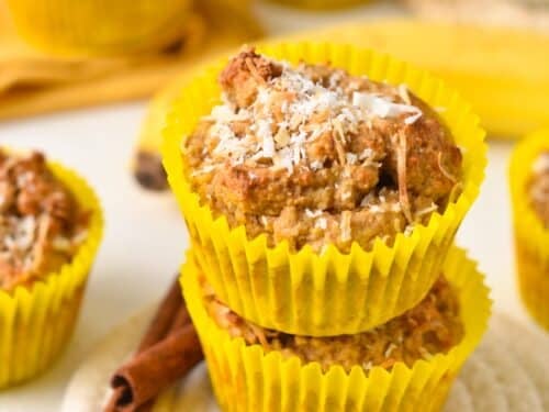 a stack of two coconut flour banana muffins with yellow muffin paper and shredded coconut on top