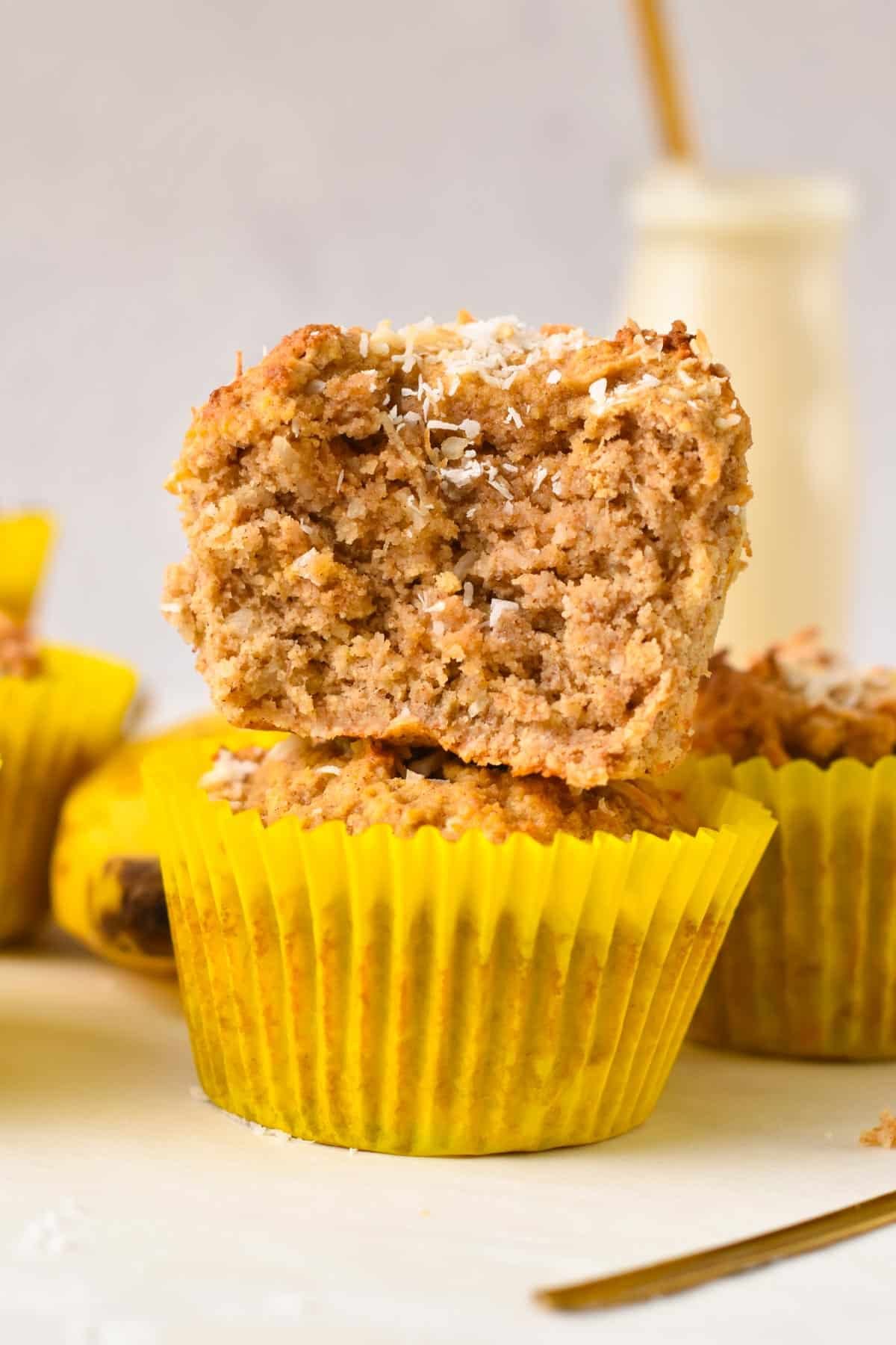 A stack of two coconut flour banana muffins with the one one top half bitten showing the light, fluffy muffin crumbs.
