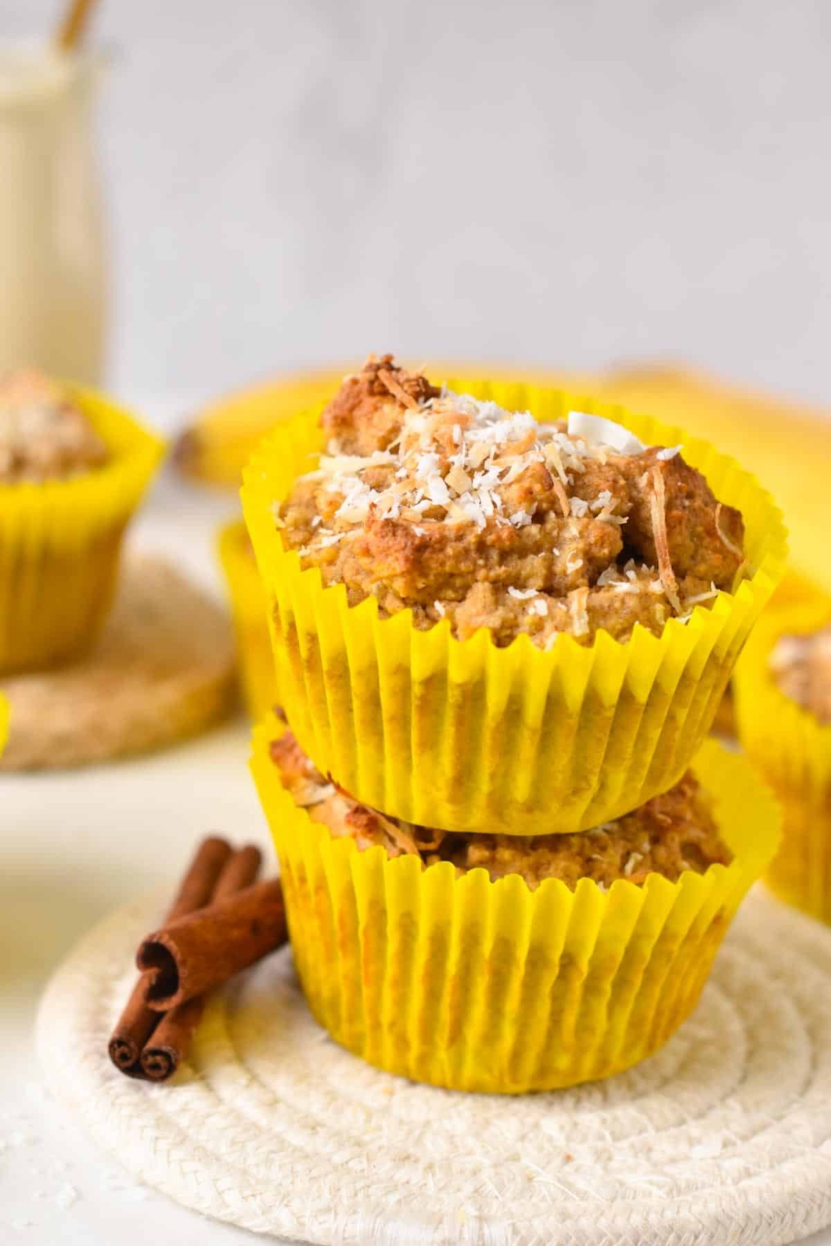 Two coconut flour banana muffins with yellow muffin paper and shredded coconut on top.