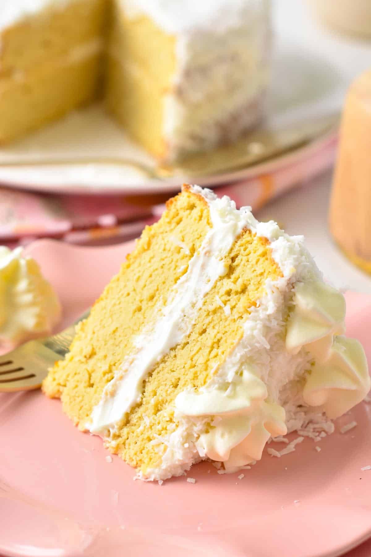 A slice of two layer This Coconut Flour Cake is a moist, fluffy gluten-free, low-carb birthday cake for coconut lovers. You will love its light coconut crumb filled with vanilla frosting.  with white frosting and shredded coconut around.