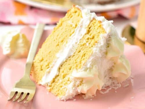 a slice of two layer This Coconut Flour Cake is a moist, fluffy gluten-free, low-carb birthday cake for coconut lovers. You will love its light coconut crumb filled with vanilla frosting. with white frosting and shredded coconut around