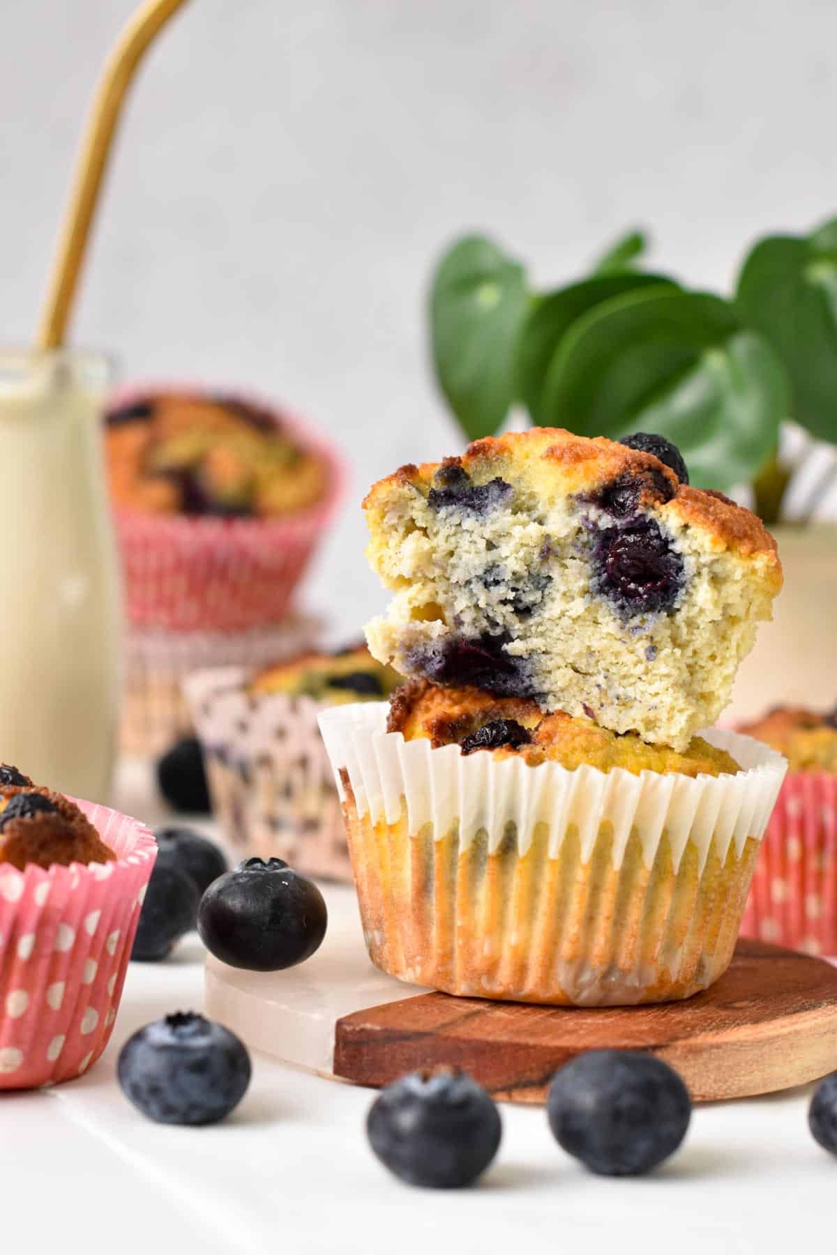 Two coconut flour blueberry muffins stacked together with the one on top half sliced showing the moist, fluffy texture of the muffin.