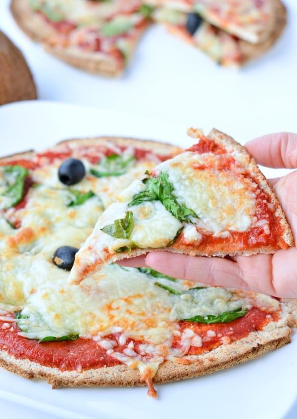 A slice of Coconut Flour Pizza with mozzarella, basil, and tomato sauce in front of the whole pizza.