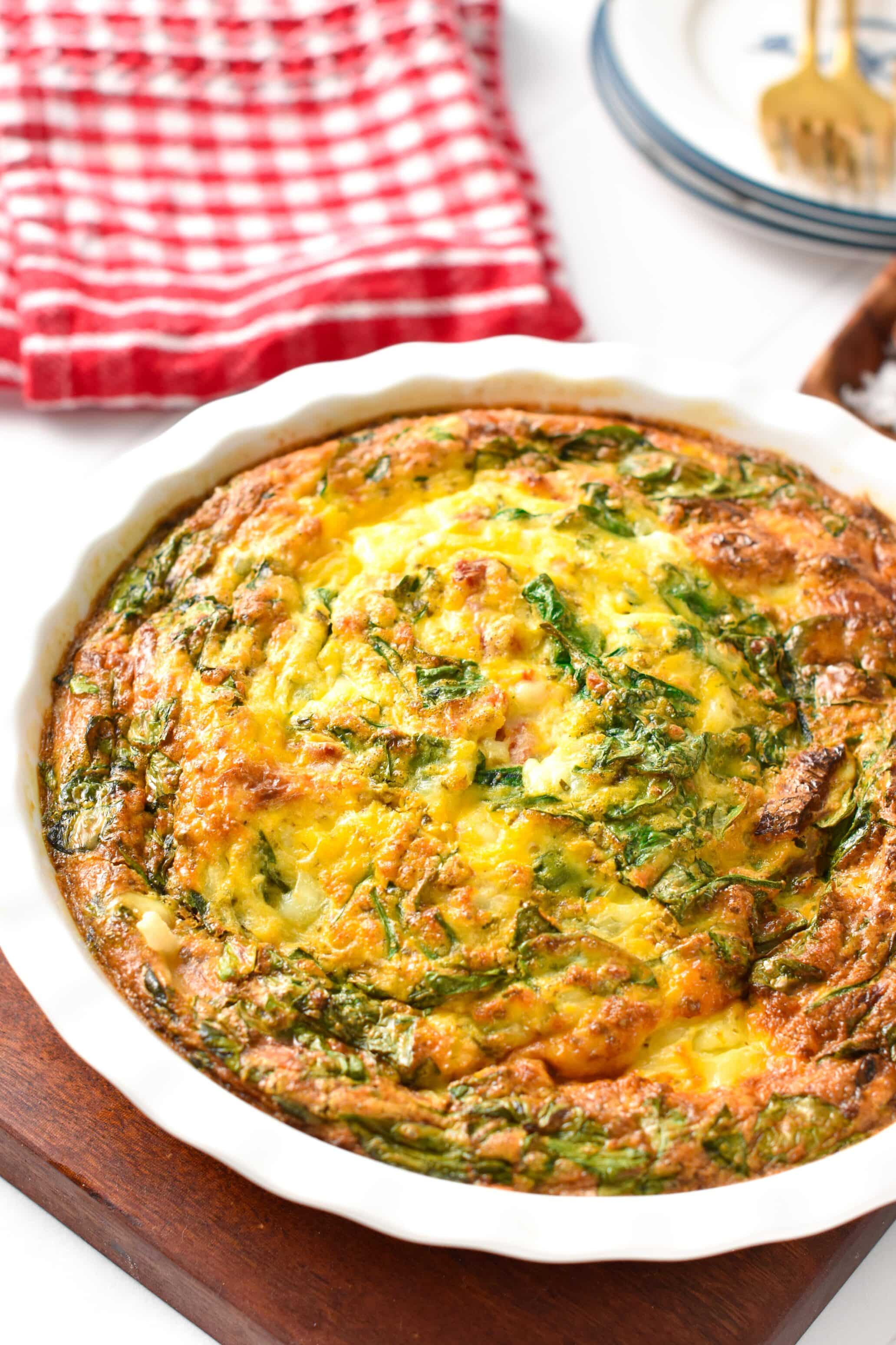 A cottage cheese egg bake in a pie plate filled with spinach, sundried tomatoes and cheddar.