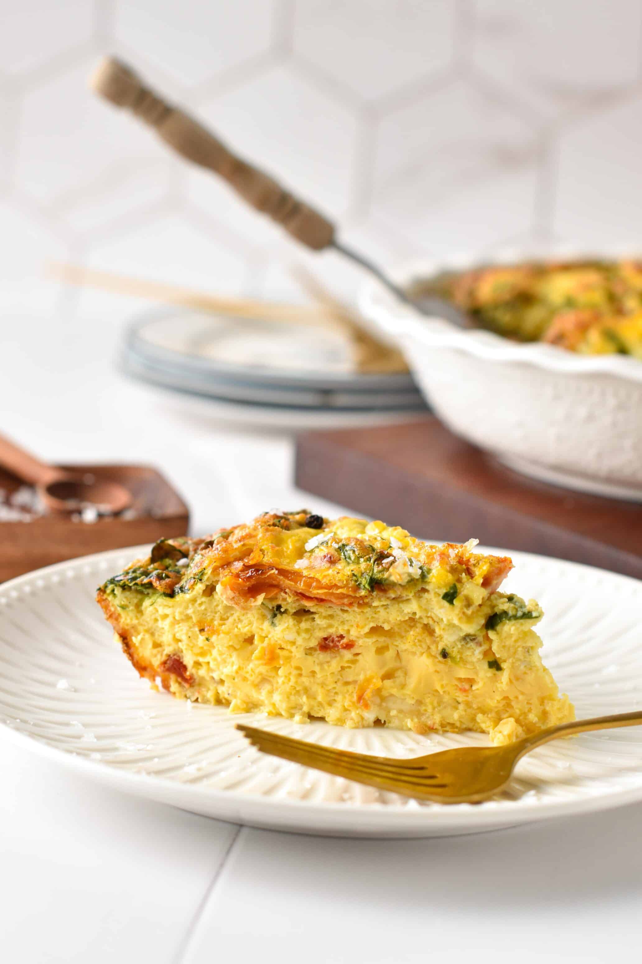 A slice of egg bake in a plate with cottage cheese, spinach, cheese, sundried tomatoes.