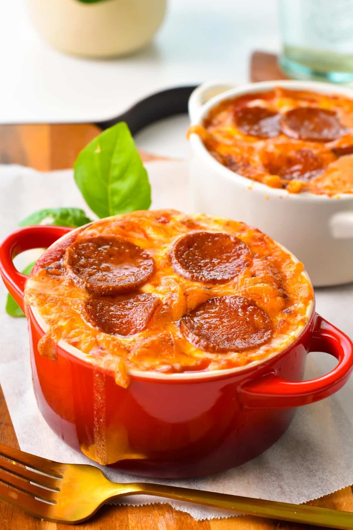 A red ramekin with baked cottage cheese, grated grilled mozzarella and pepperoni slices.