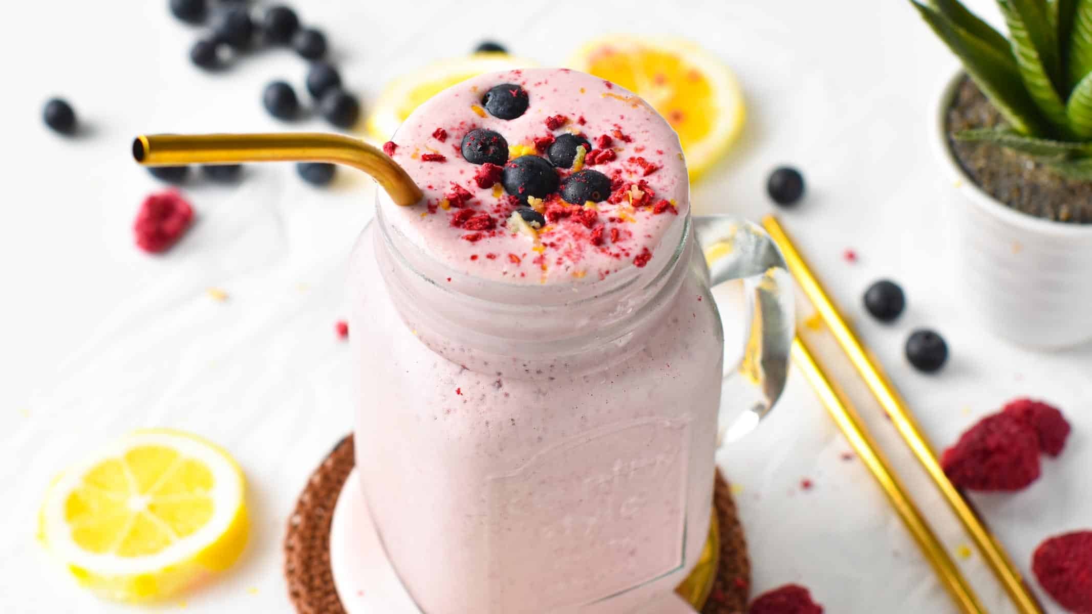 Cottage Cheese Protein Shake in a jar decorated with blueberries and raspberry powder, and a golden straw.