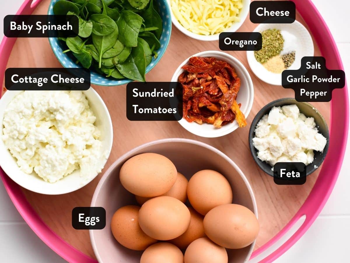 Cottage cheese Egg Bake ingredients on a tray including picture of ingredients in small bowls : eggs, feta, cheese, spinach, cottage cheese, dried oregano, garlic powder, salt and pepper.