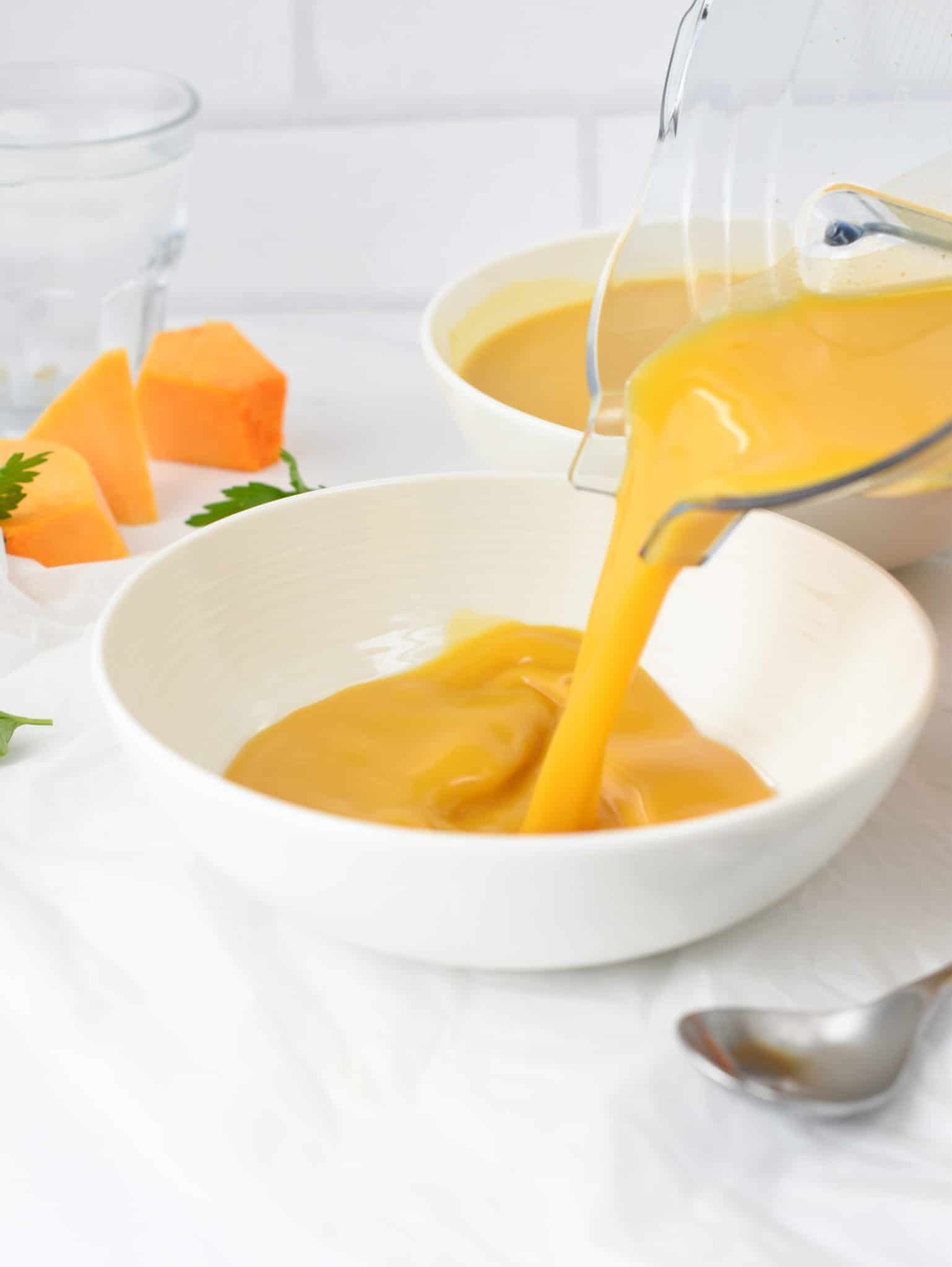 Pouring Creamy keto pumpkin soup into a large bowl.