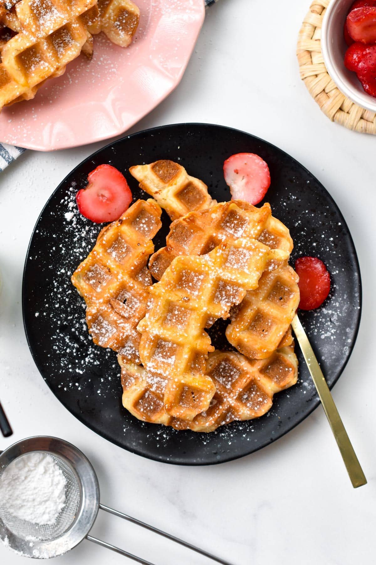 Croffles stacked on a black plate with a dust of powdered sugar.