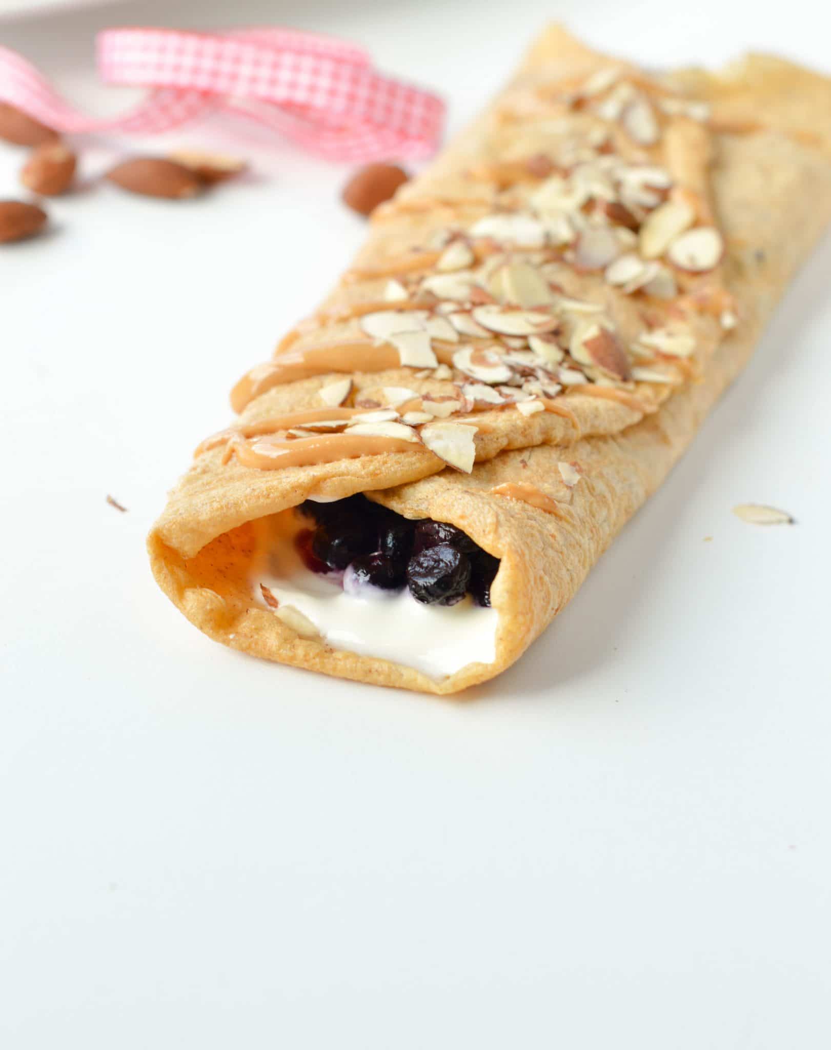 Almond Flour Crepes rolled and stuffed with cream and blueberries, sprinkled with almond slices.