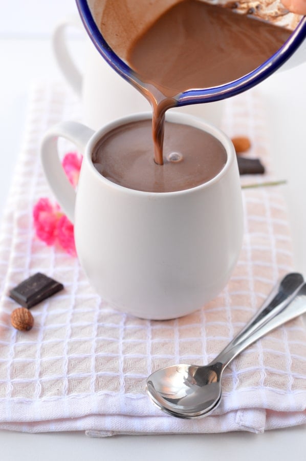 Pouring keto hot chocolate from a saucepan to a mug on a kitchen towel.