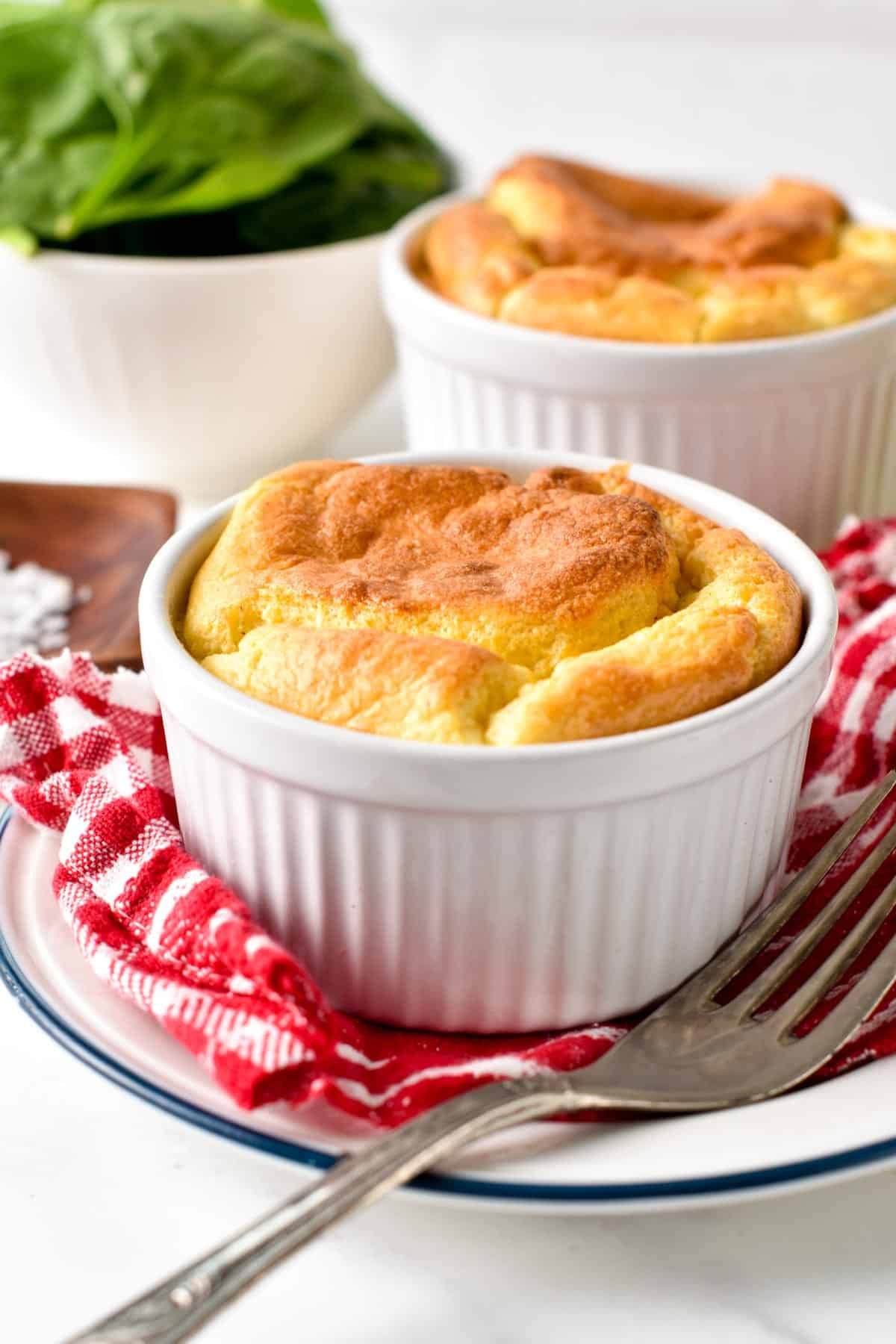 Egg souffle in a small ramekin on a plate lined with a checkered kitchen towel.