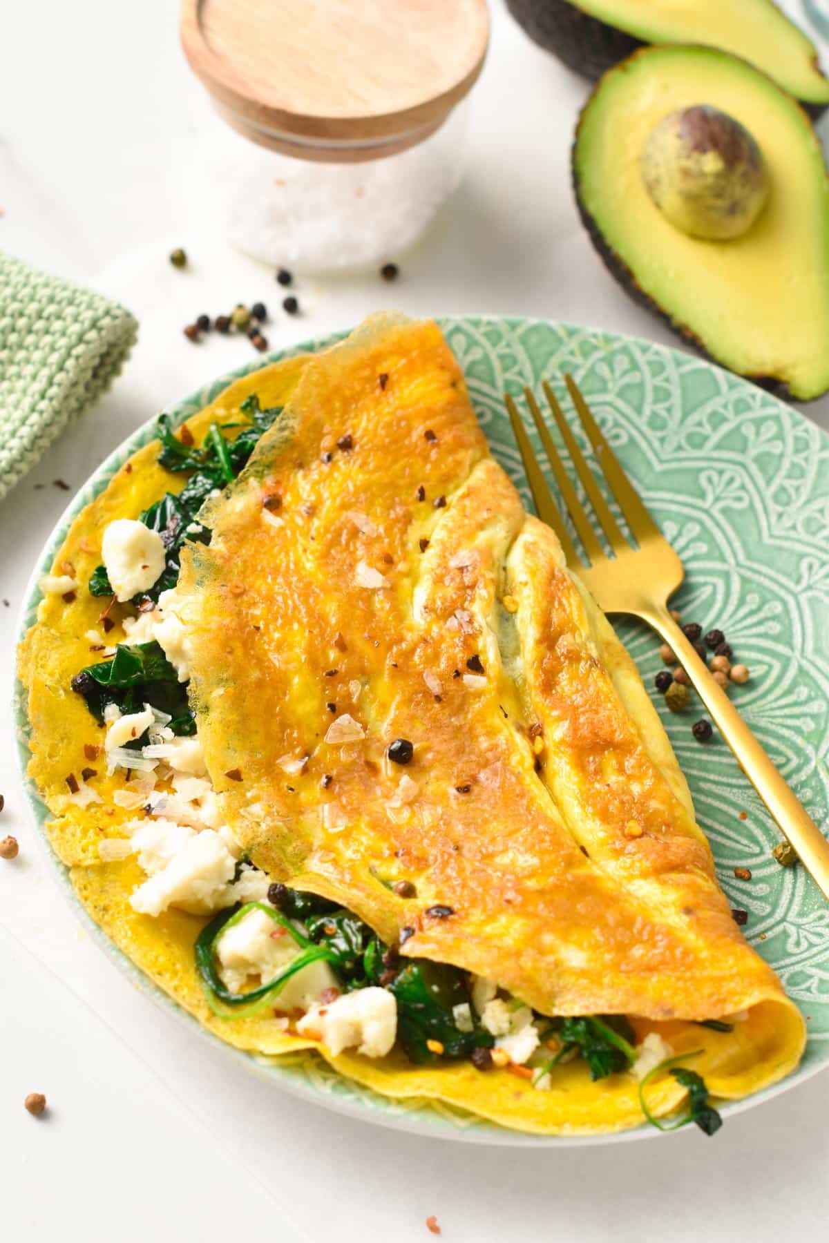 A green plate with a feta spinach omelette on it and a golden fork on the right side.