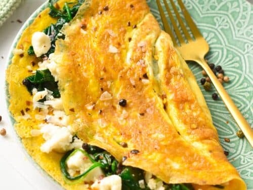 a green plate with a feta spinach omelette on it and a golden fork on the right side