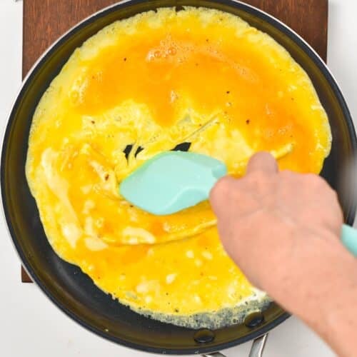 a rubber spatula pushing the sides of the omelet to let the uncooked eggs run under in the skillet