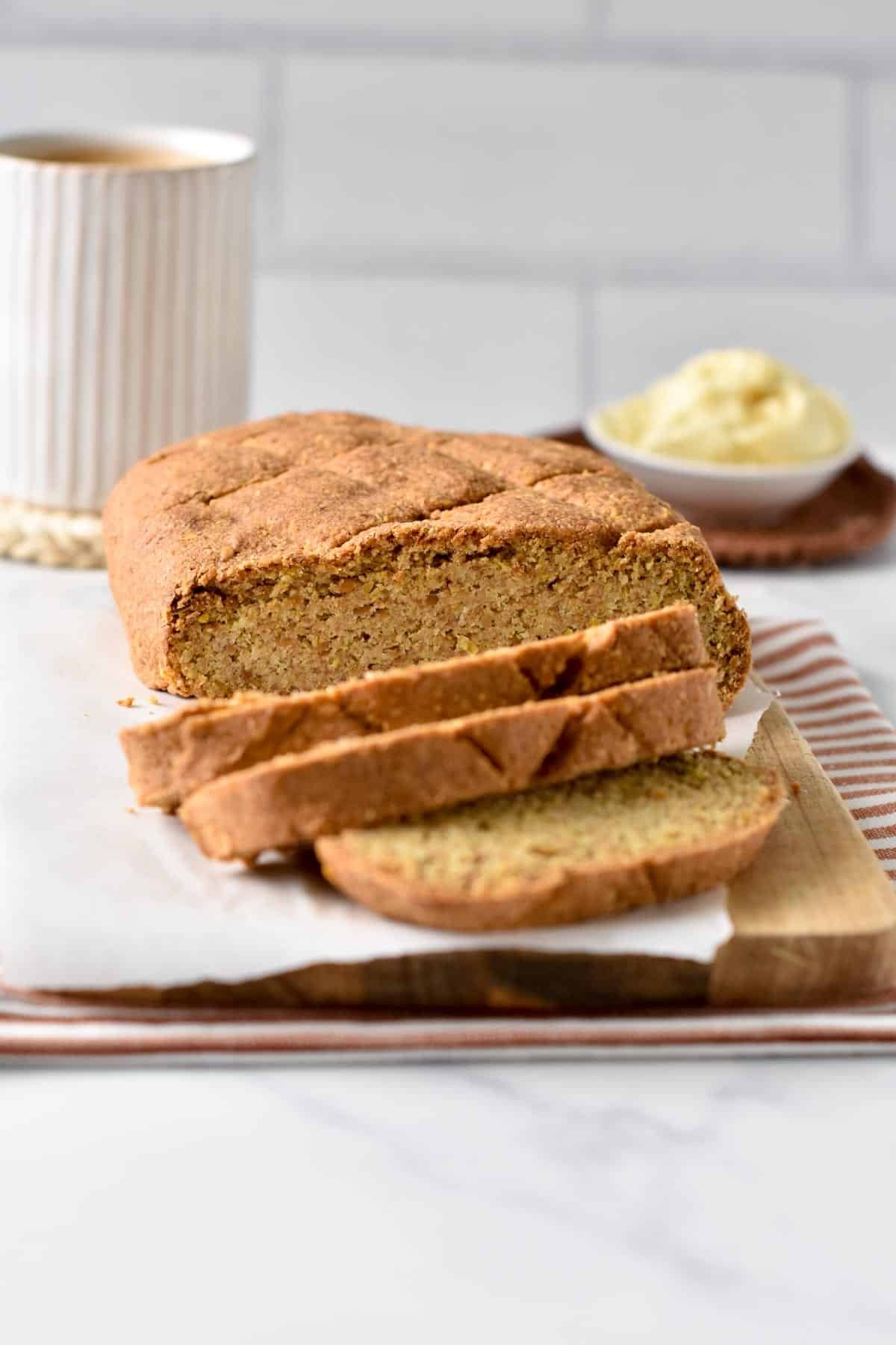 Sliced Flaxseed Bread in front of a cup with butter and a coffee mug.