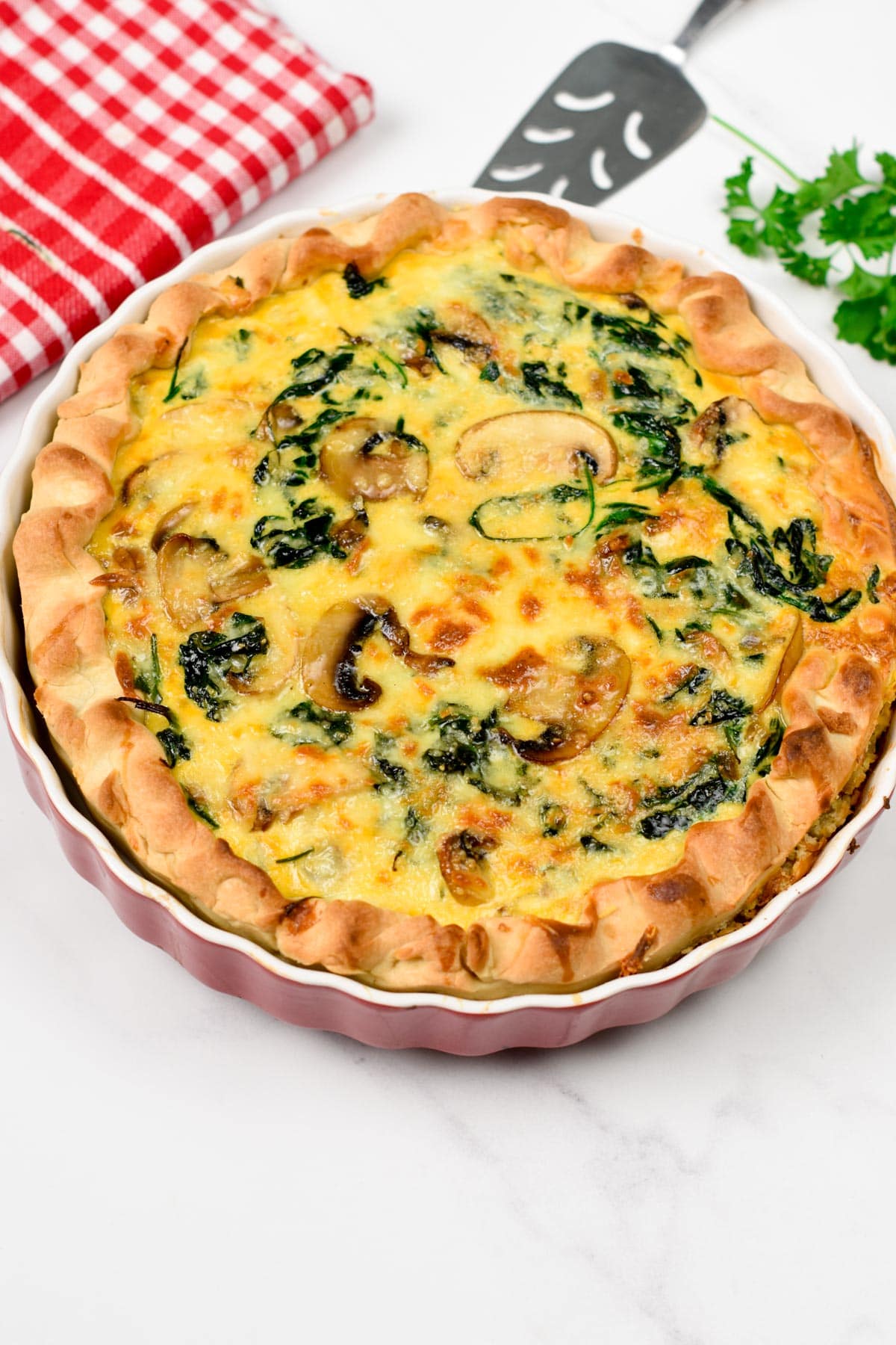 Florentine Quiche on a pie pan in front of a red tablecloth.