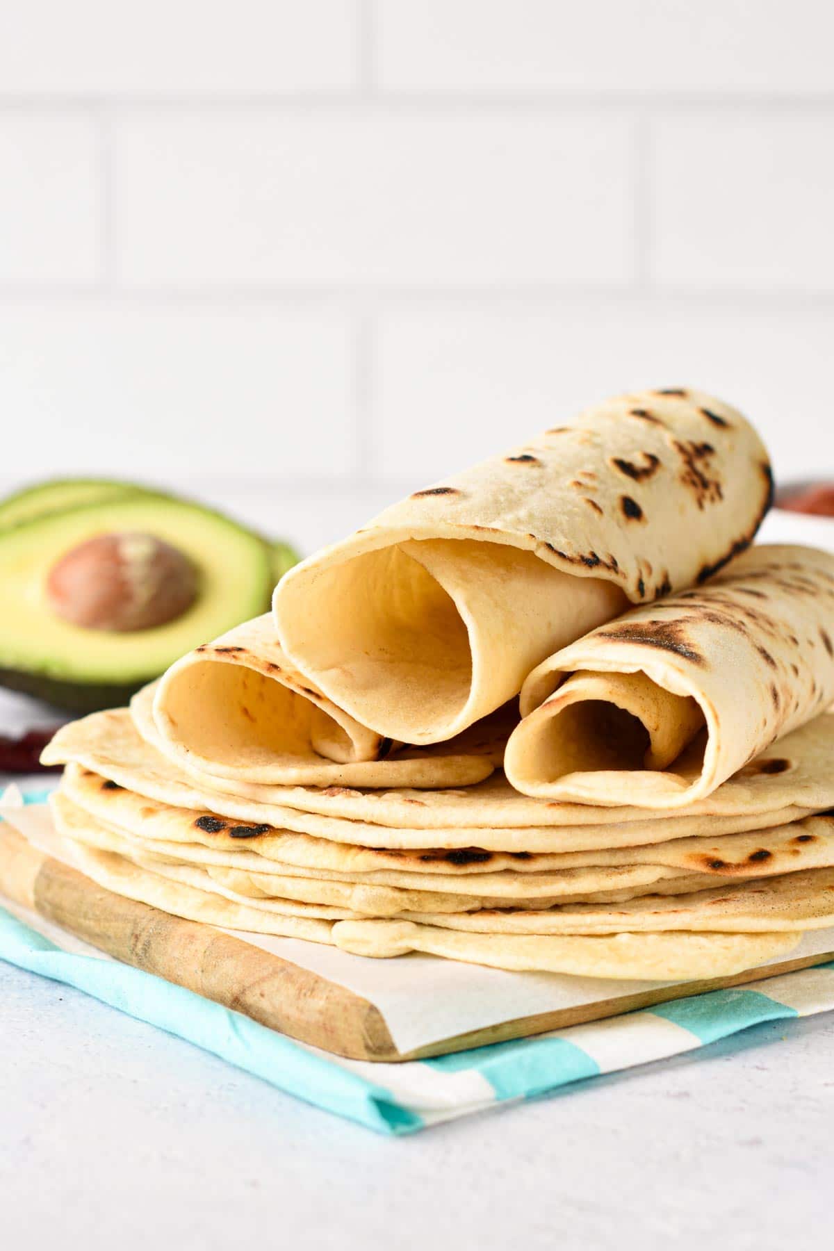 Stack of Flour Tortilla on a chopping board with the top 3 rolled.
