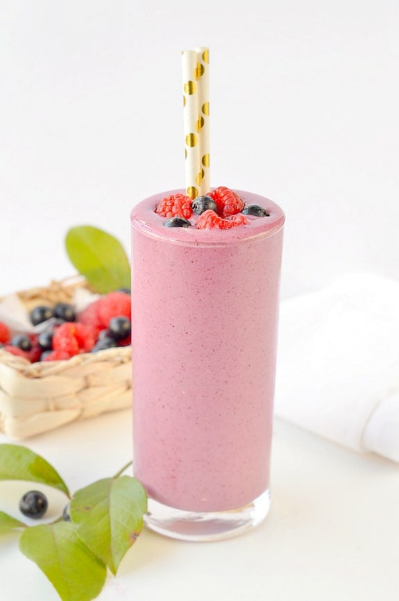 Healthy berry smoothie in a glass next to fresh berries in a ratan box.