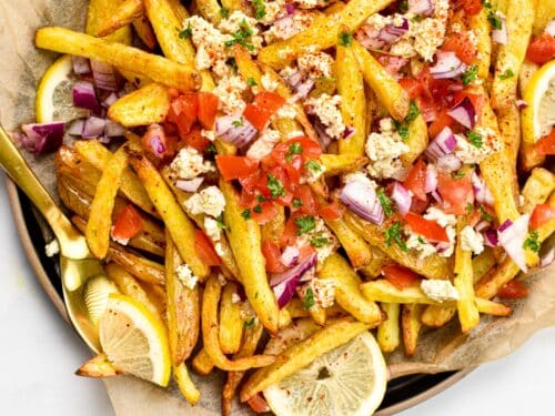 These homemade Greek Fries are crispy baked fries topped with a drizzle of lemon juice and loads of delicious Greek cuisine flavors from feta cheese, red onions, tomatoes and Parsley.