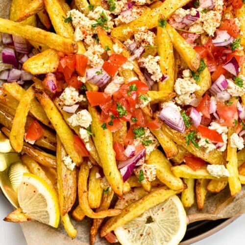 These homemade Greek Fries are crispy baked fries topped with a drizzle of lemon juice and loads of delicious Greek cuisine flavors from feta cheese, red onions, tomatoes and Parsley.