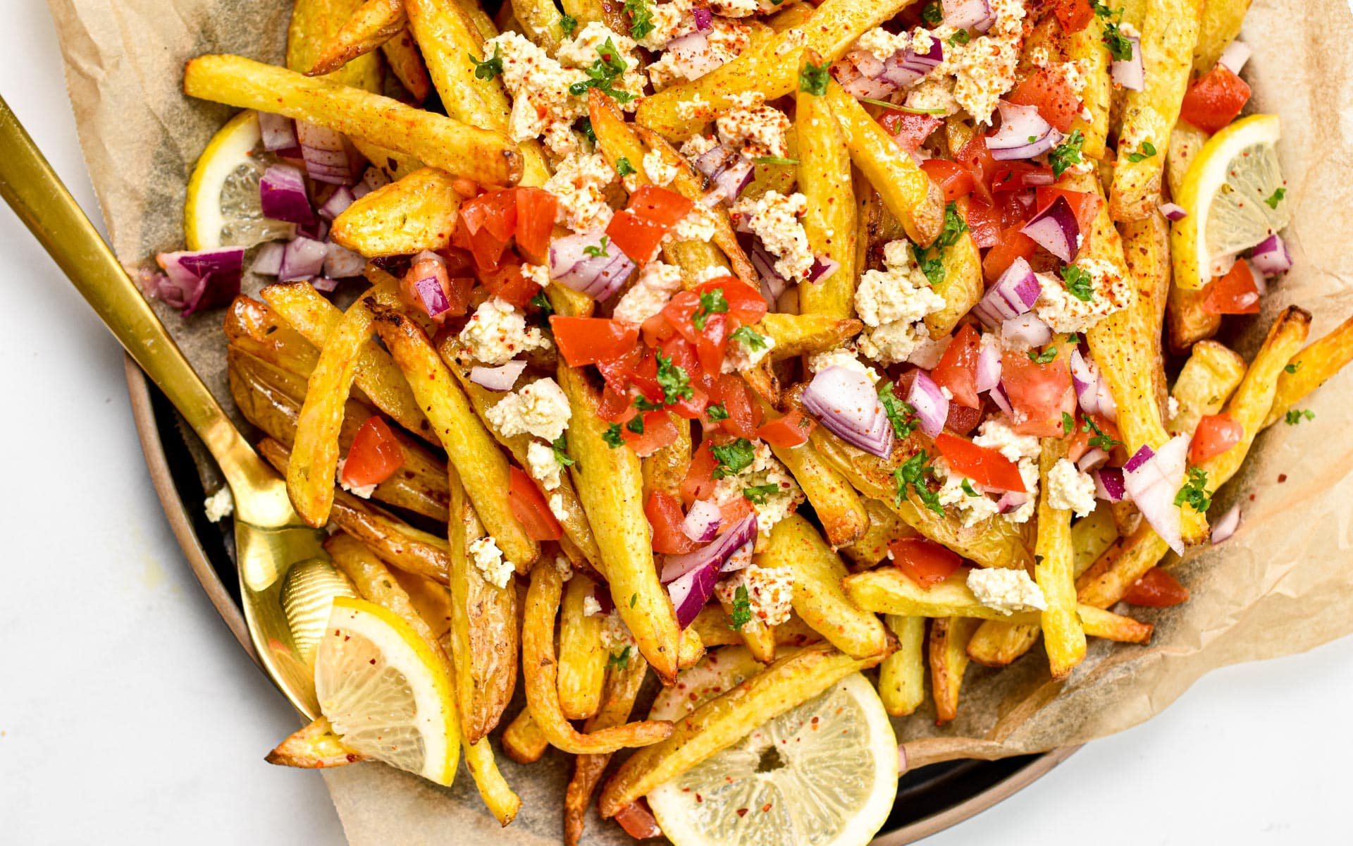 These homemade Greek Fries are crispy baked fries topped with a drizzle of lemon juice and loads of delicious Greek cuisine flavors from feta cheese, red onions, tomatoes and Parsley.