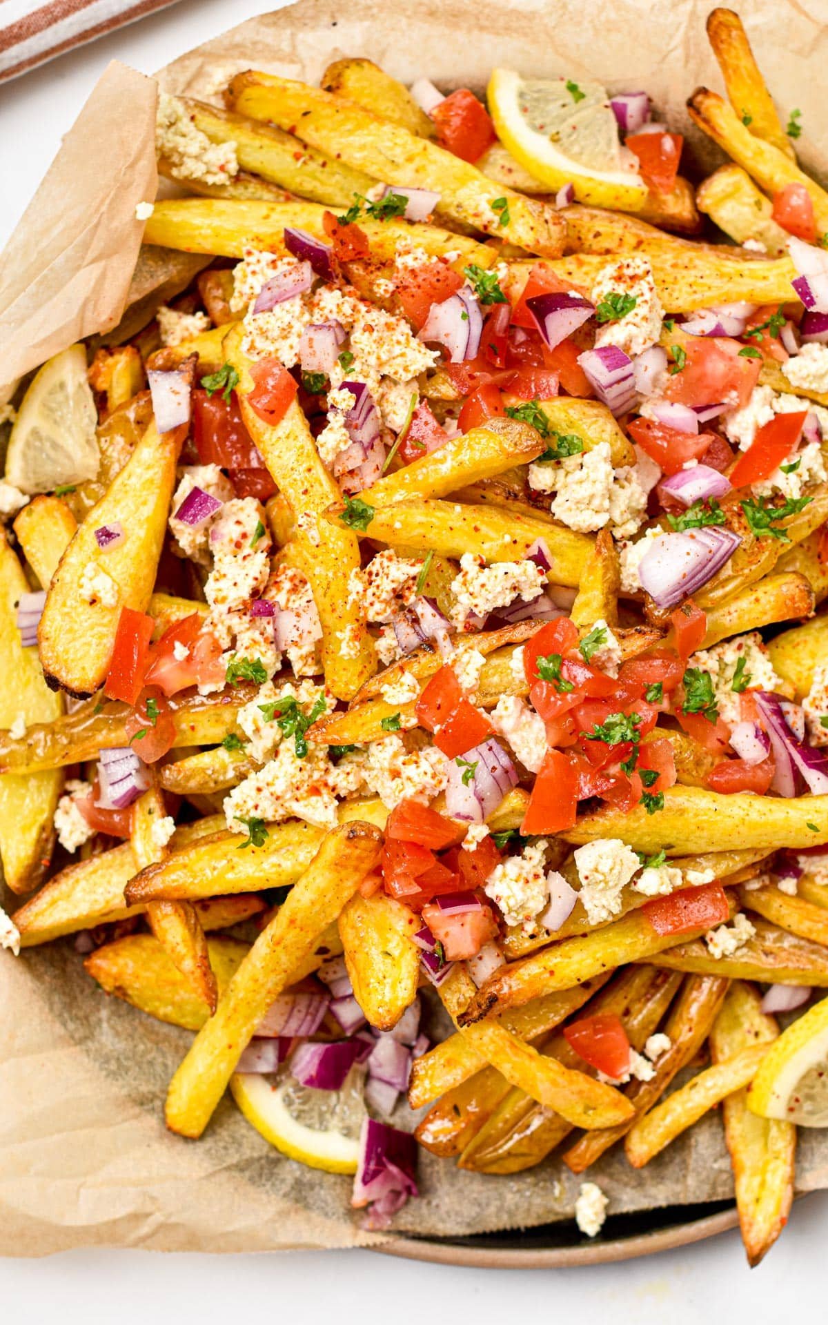 These homemade Greek Fries are crispy baked fries topped with a drizzle of lemon juice and loads of delicious Greek cuisine flavors from feta cheese, red onions, tomatoes and Parsley.