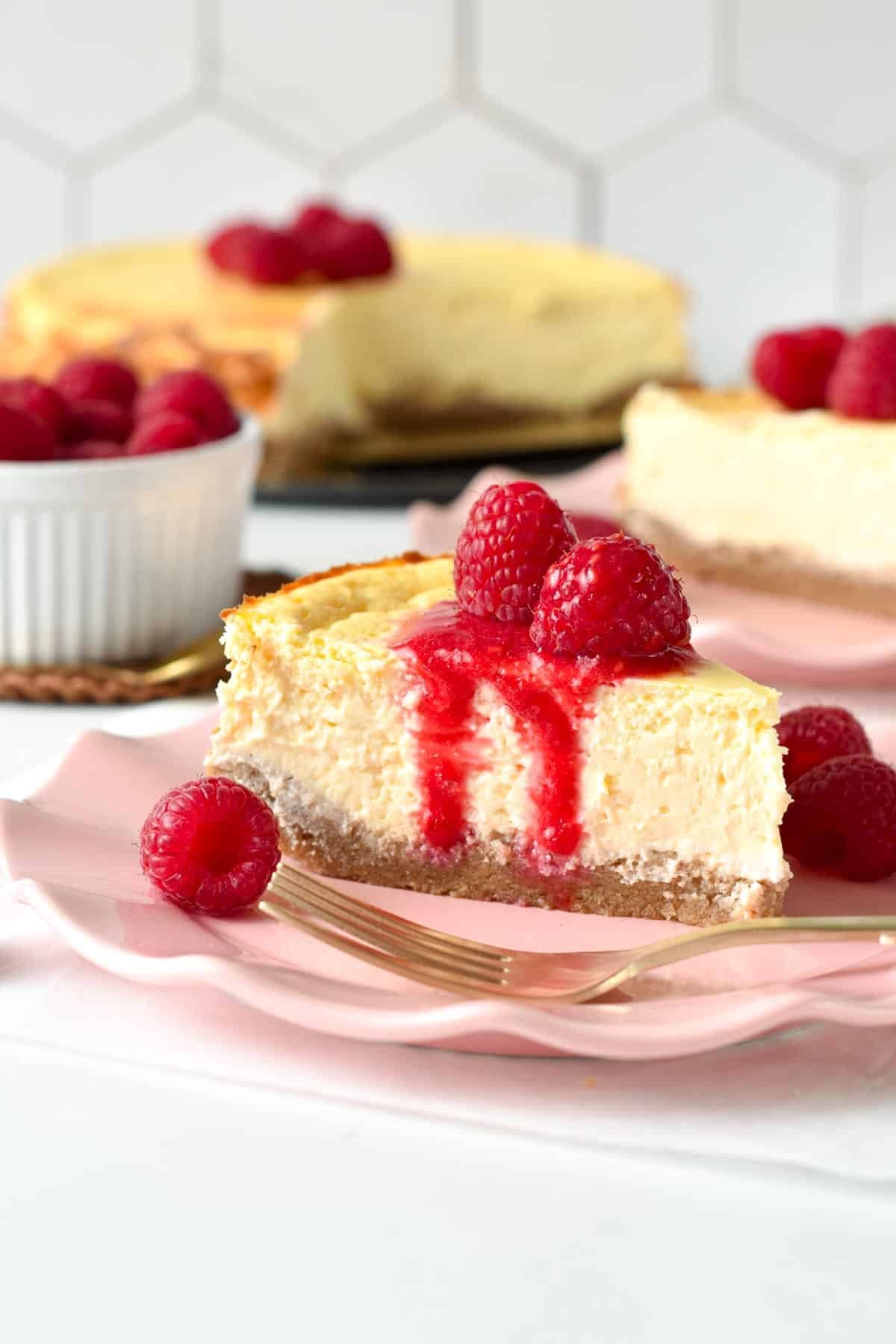 Healthy cheesecake slice on a pink plate decorated with raspberries and coulis.
