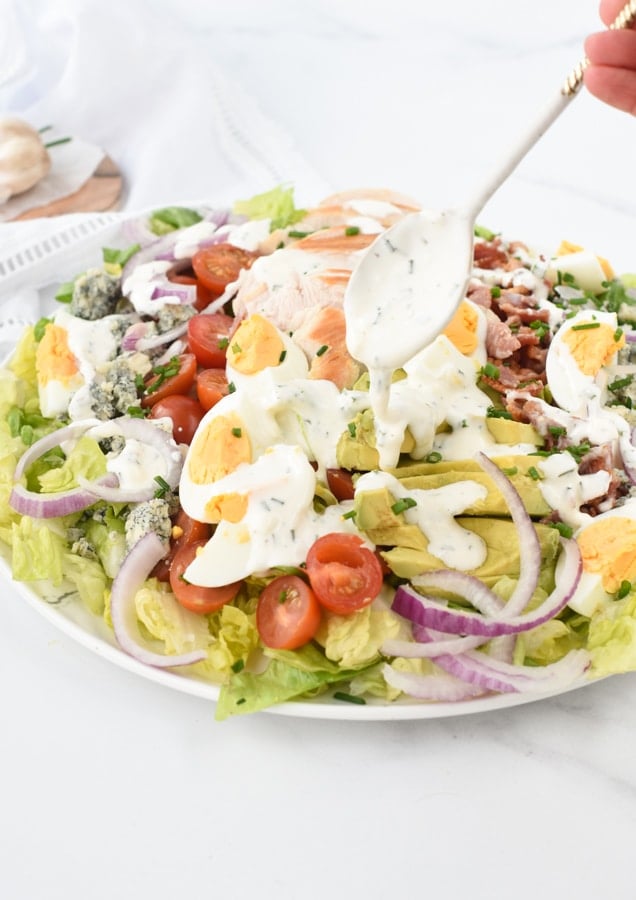 Pouring low-carb vinaigrette on top of a healthy cobb salad in a large plate.
