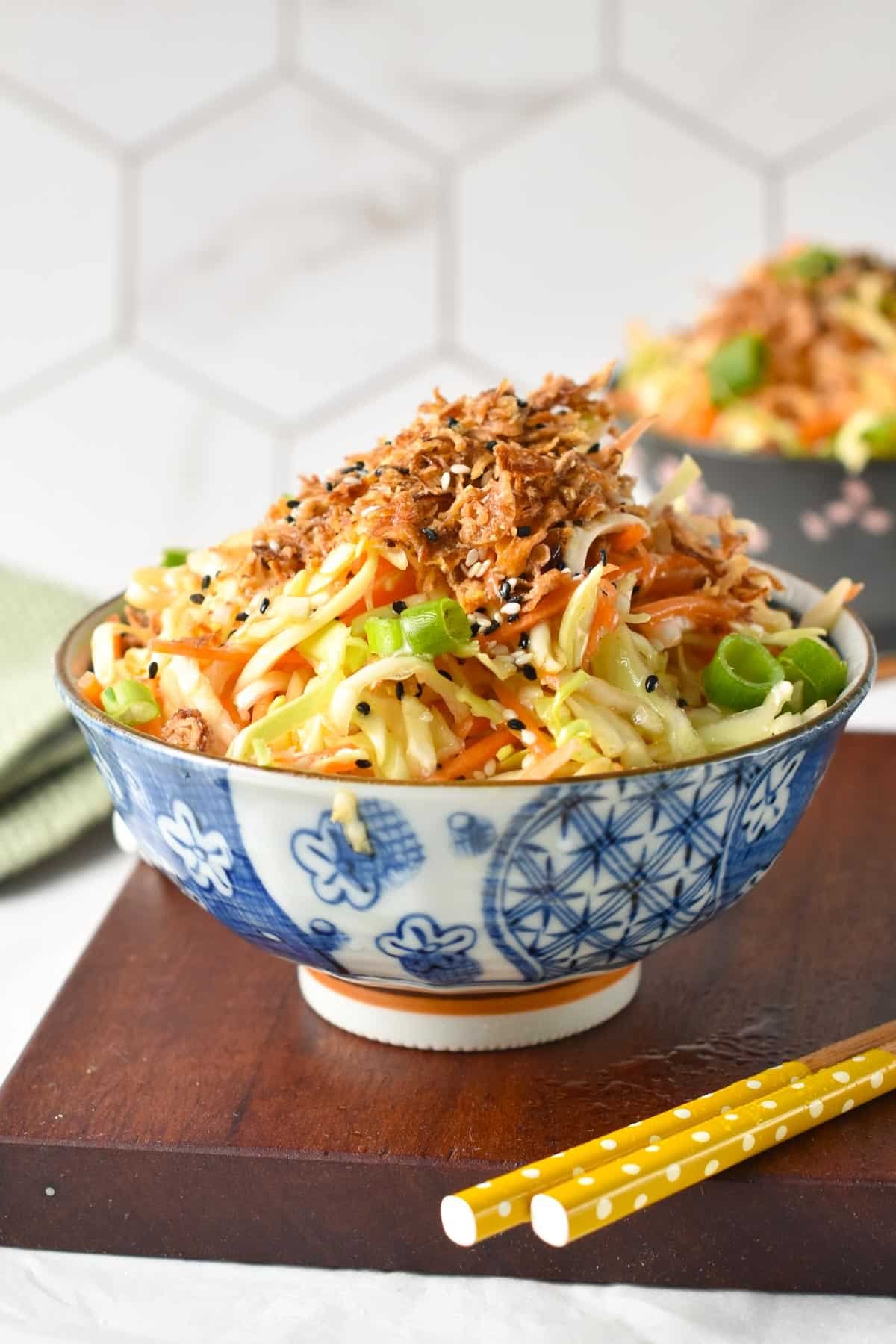A bowl of Japanese cabbage salad topped with fried shallots on a wooden board with chopsticks.