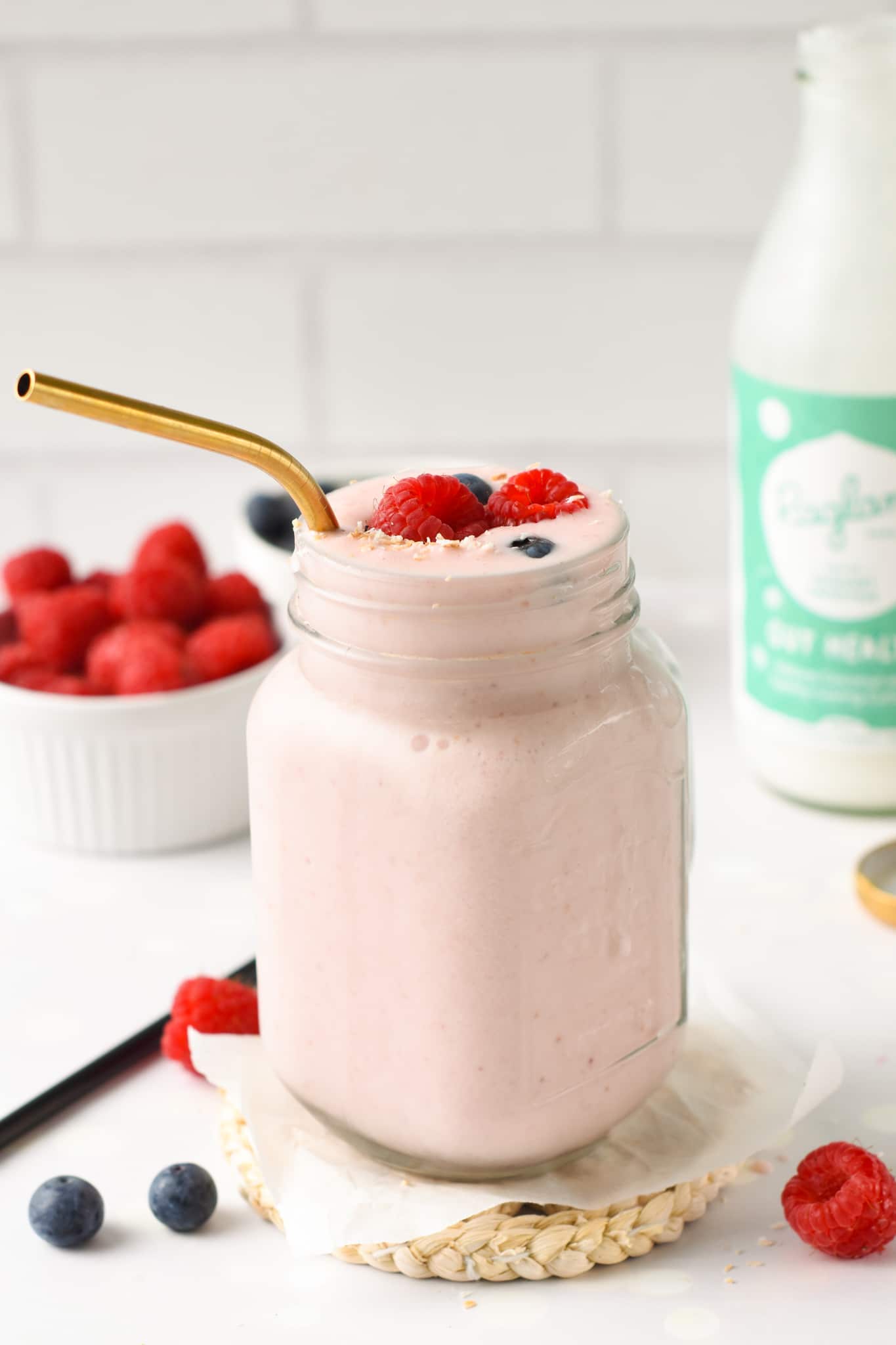 Kefir Smoothie in a large glass container decorated with raspberries and blueberries and with a golden spoon.