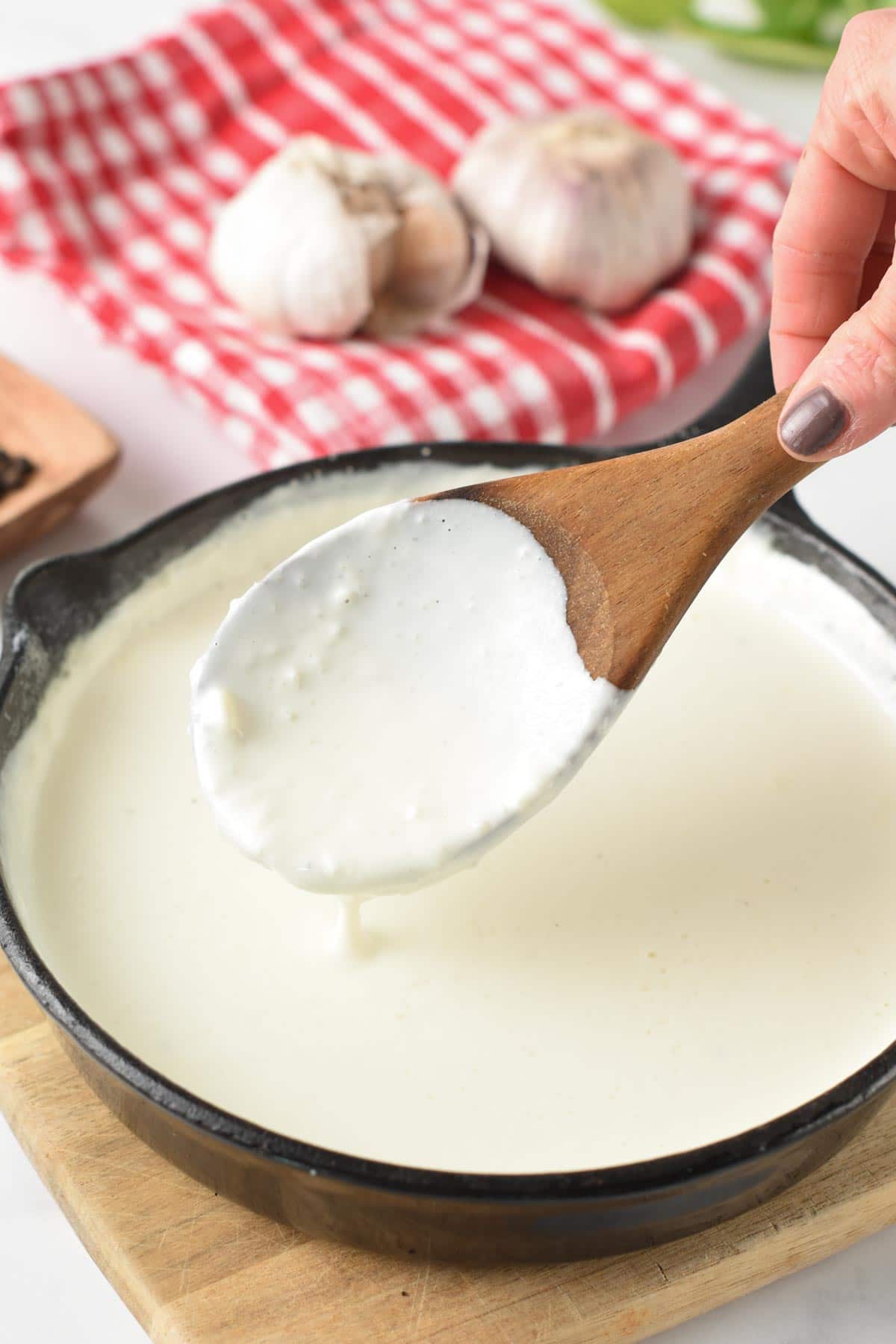 3 ingredient Alfredo Sauce in a pan and wooden spoon.