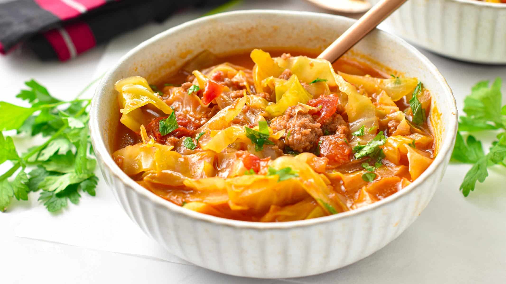 A bowl filled with low-carb cabbage soup made with green cabbage, beef broth, ground beef and celery and topped with fresh parsley