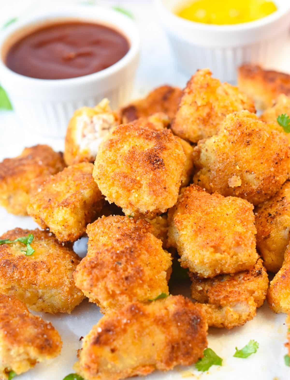 A plate filled with a stack of keto nuggets with ketchup and Dijon mustard in the background.