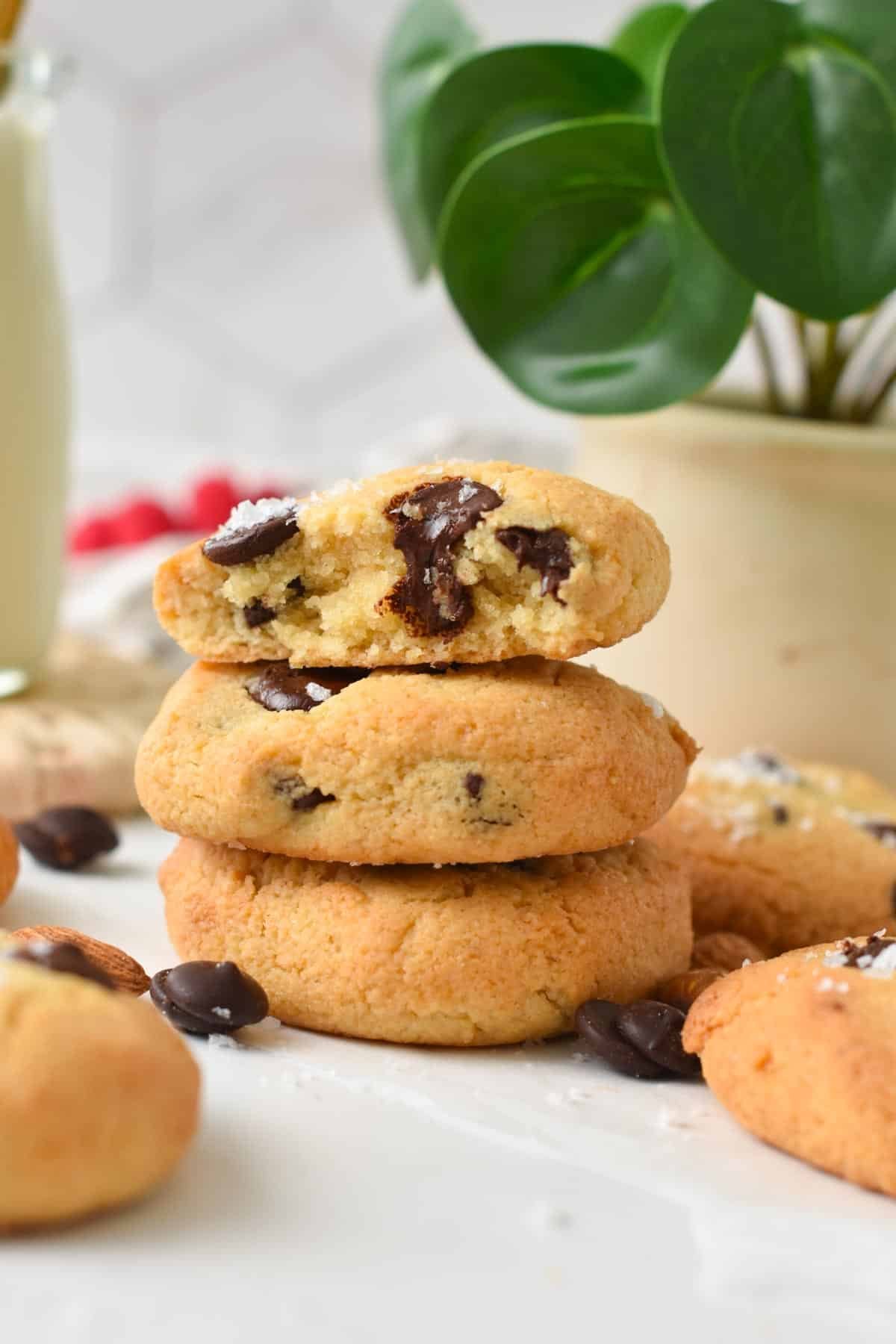 A stack of three Keto Chocolate Chip Cookies made with almond flour and the top cookie half broken showing the soft cookie texture.