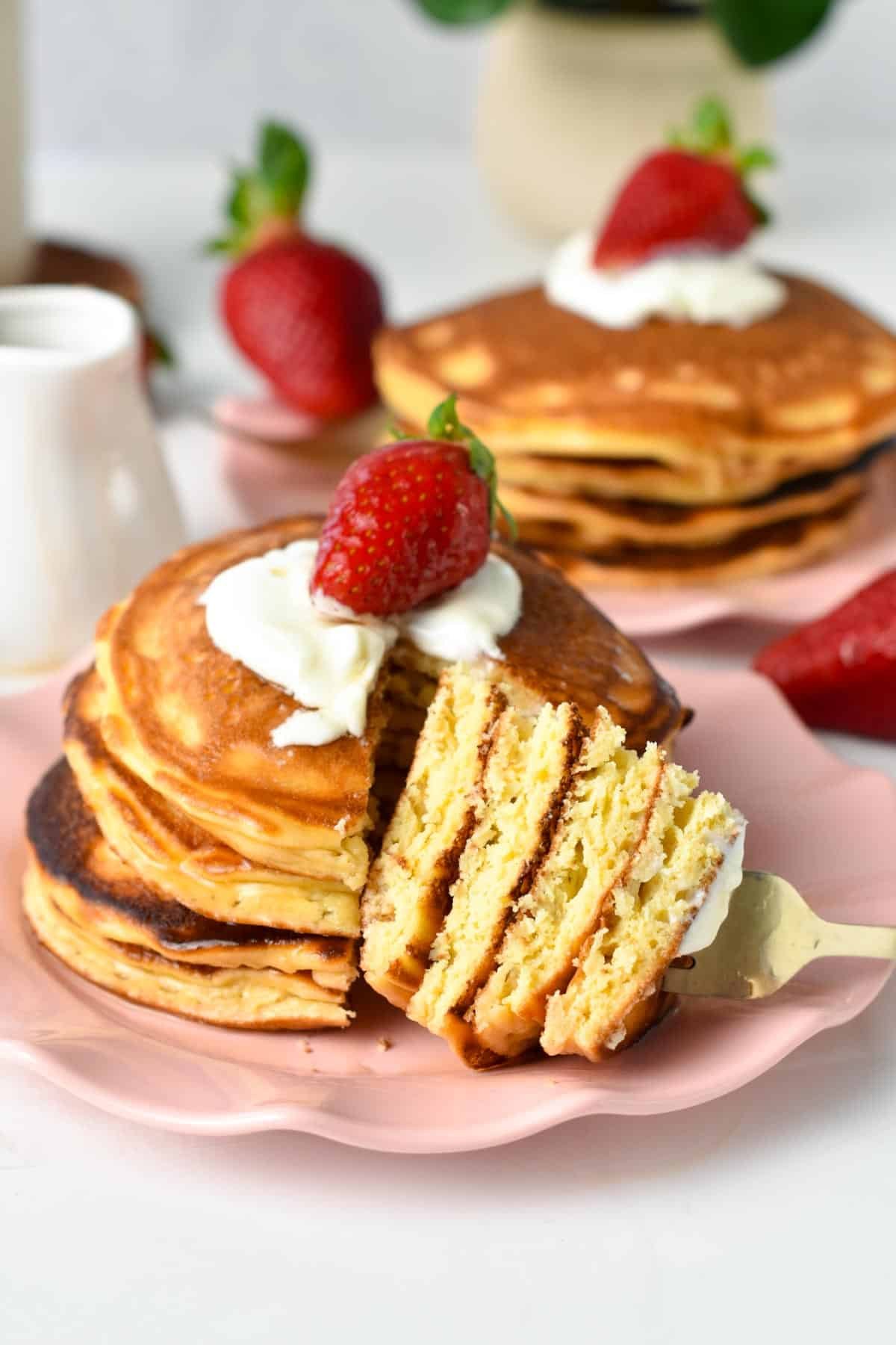 A pink plate with a stack of cottage cheese pancakes, cut and showing the fluffy texture inside.
