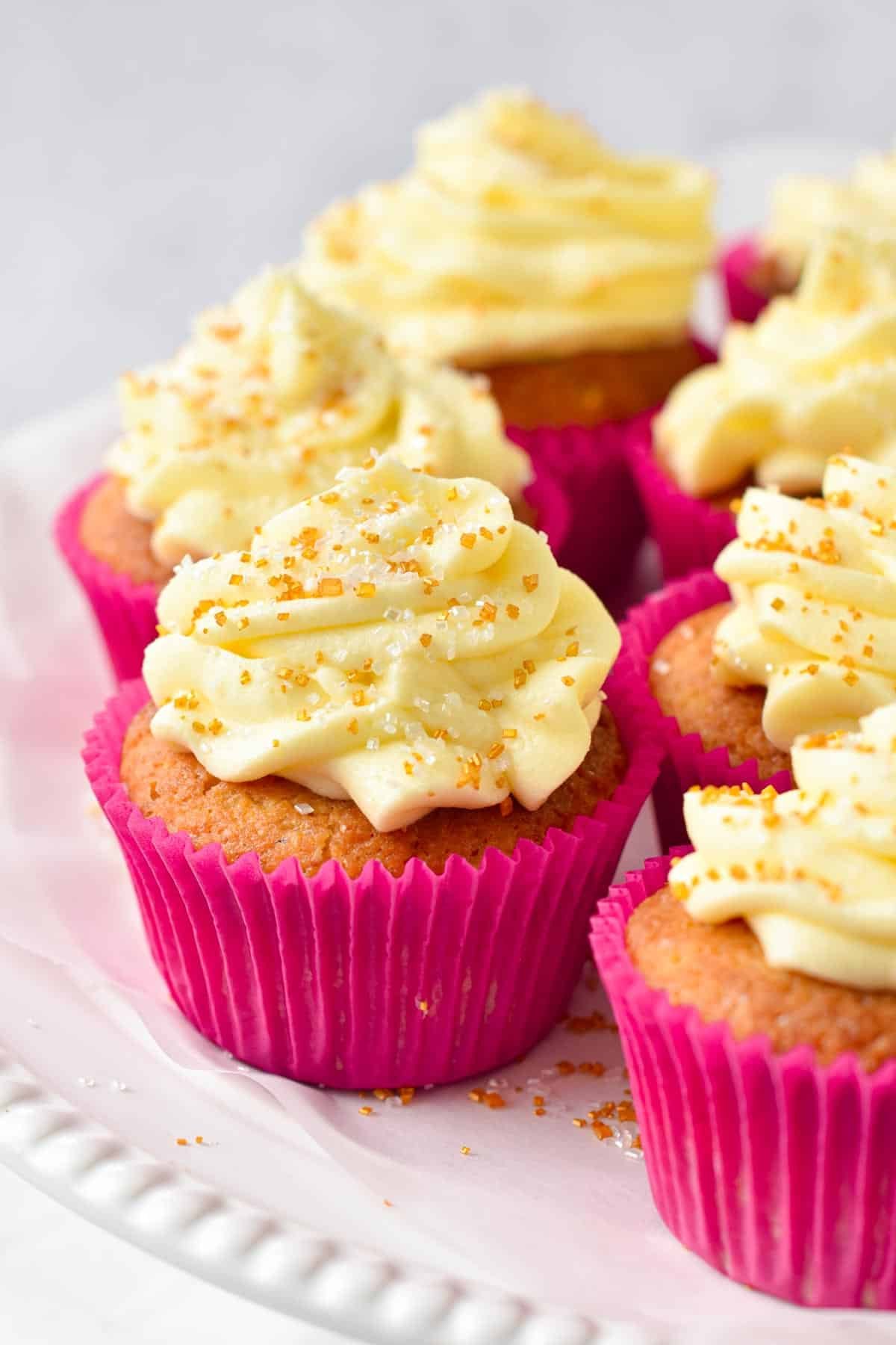 A plate filled with keto cupcakes in pink paper liners and frosted with cream cheese frosting.