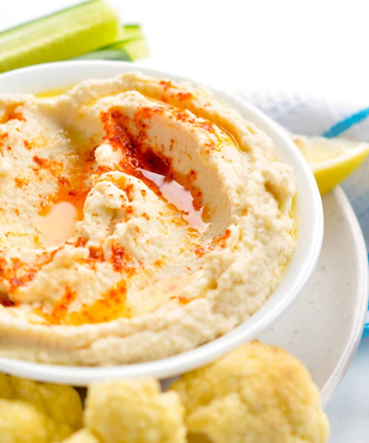 A bowl filled with keto hummus topped with olive oil and paprika with fresh vegetables around it.