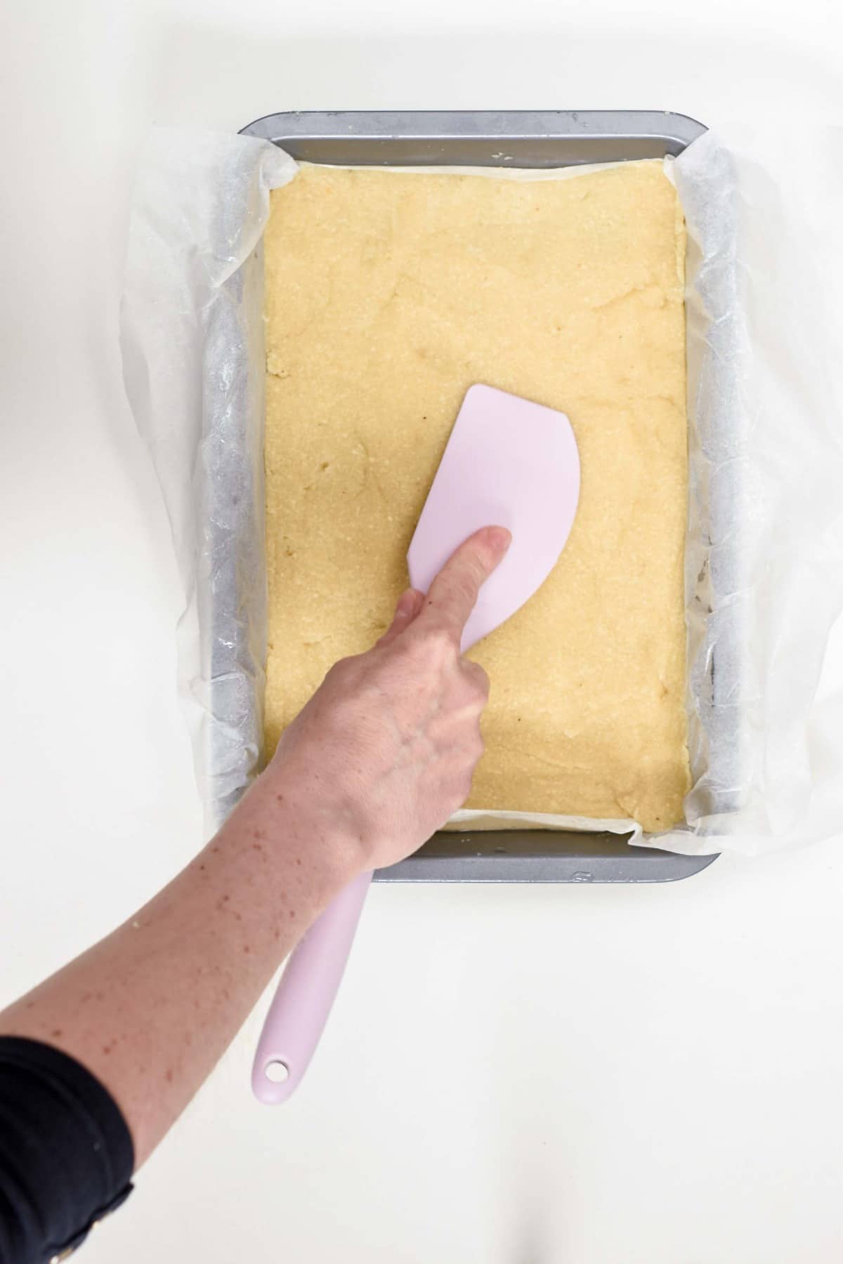 Pressing the base layer of a keto magic cookie bar on a large baking pan with a silicone spatula.